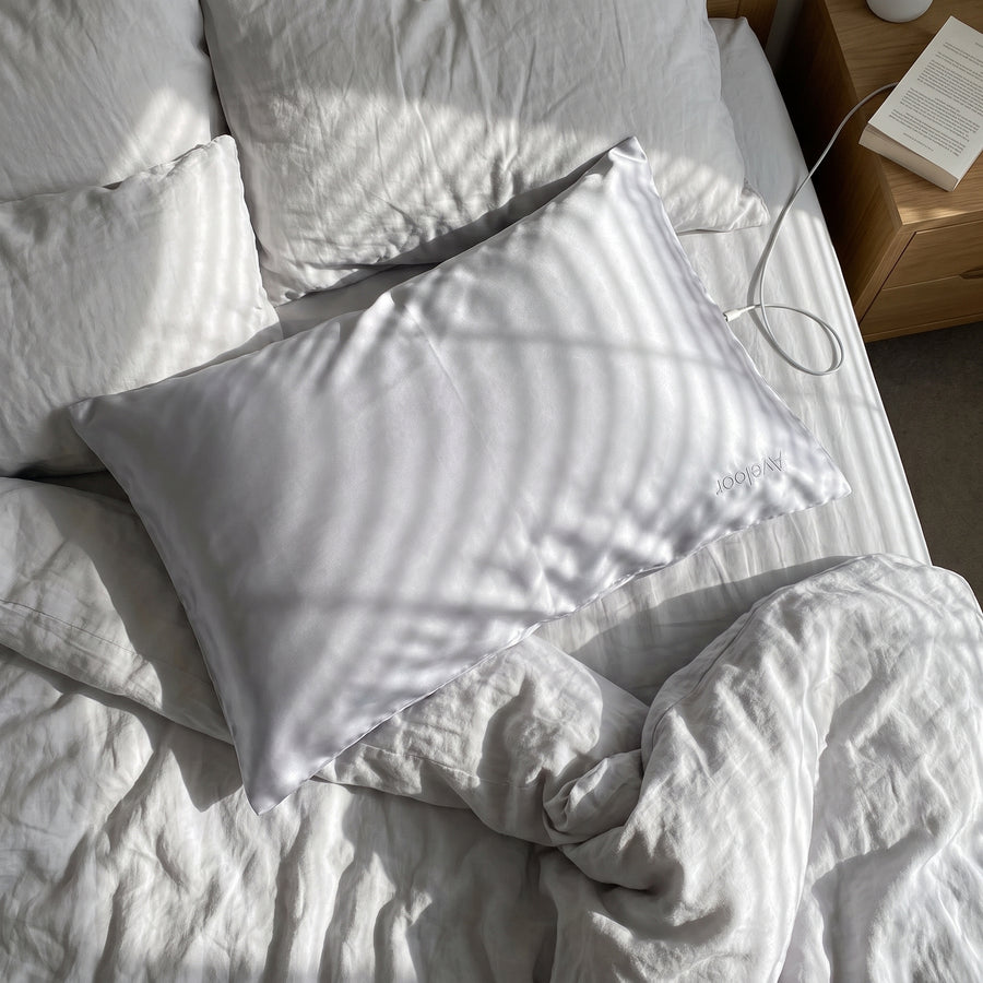 Aveloor dove silk pillowcase on a bed in soft morning light