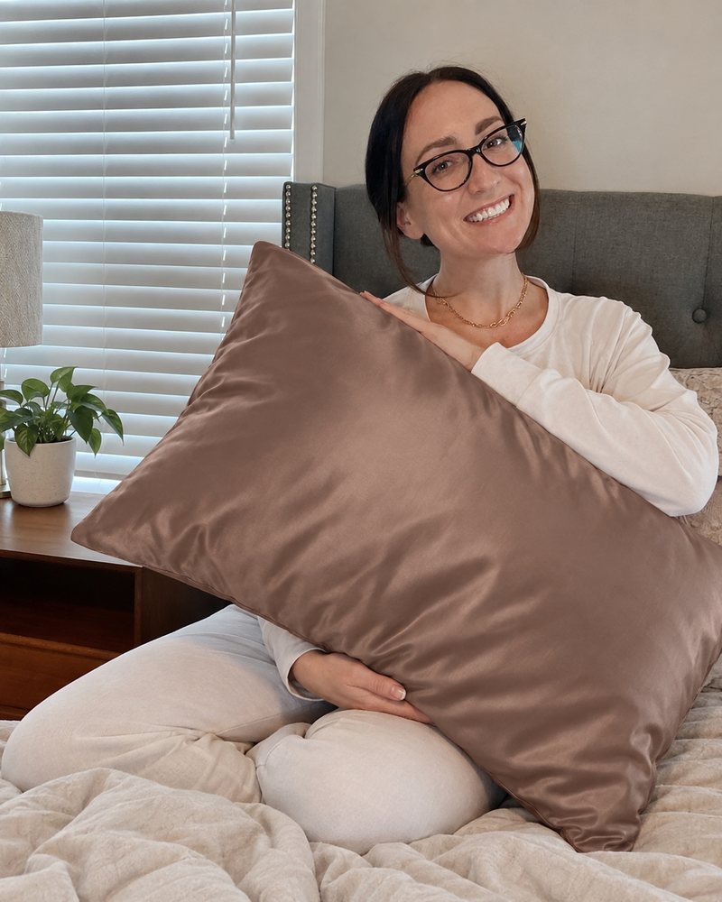 A smiling woman in glasses holding an Aveloor mulberry silk pillowcase in Cocoa