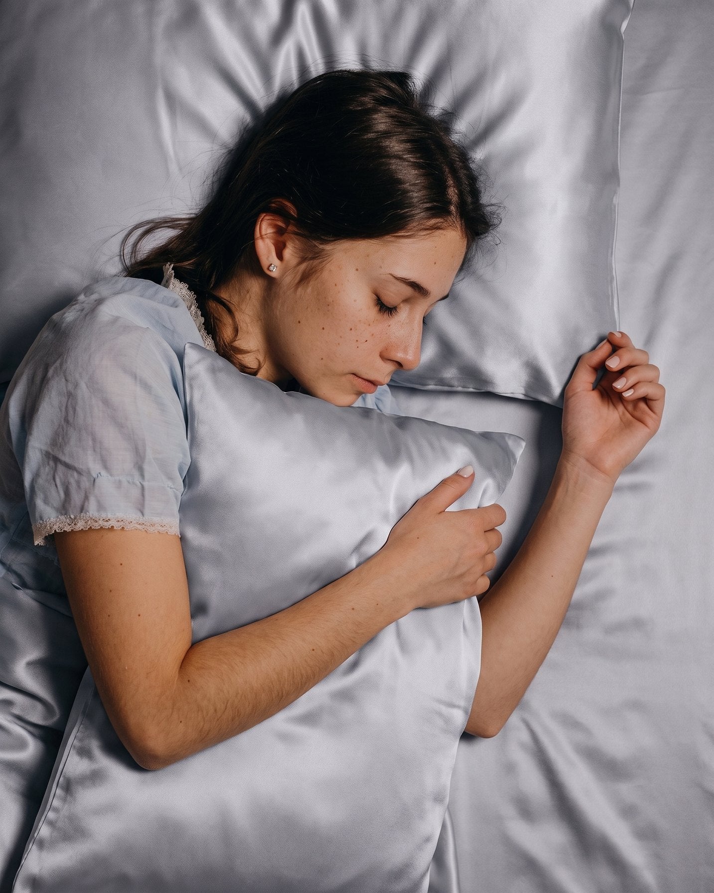 A woman asleep on her side hugging an Aveloor Dove silk pillowcase